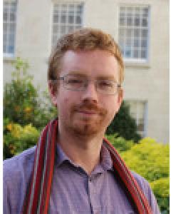 Man wearing glasses, purple shirt, and multi-coloured scarf stares at the camera.