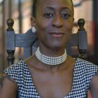 a woman stares into the camera. She is wearing a black and white shirt as well as a pearl choker and large pearl earrings